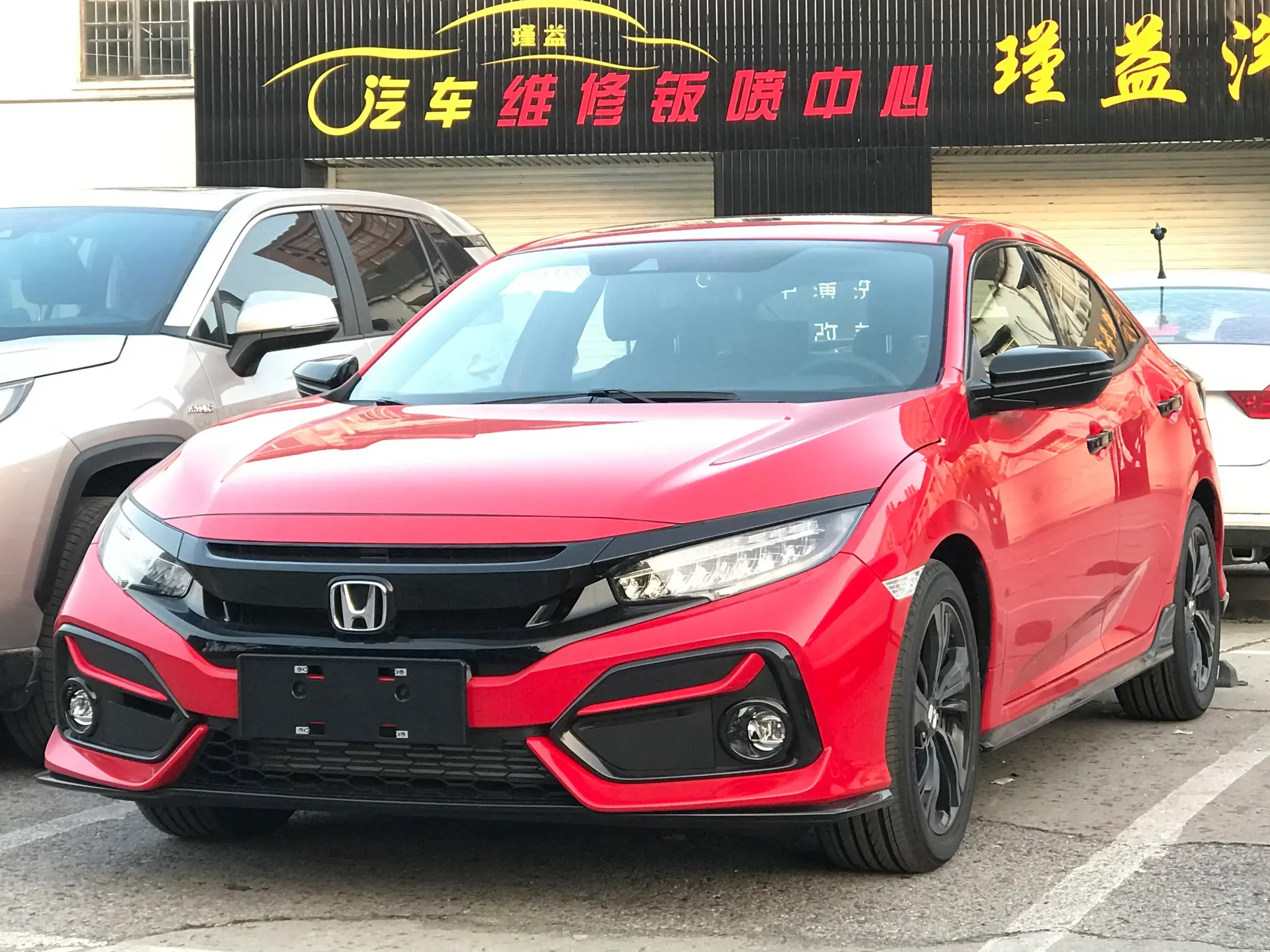 A red Honda Civic hatchback parked in front of a car workshop